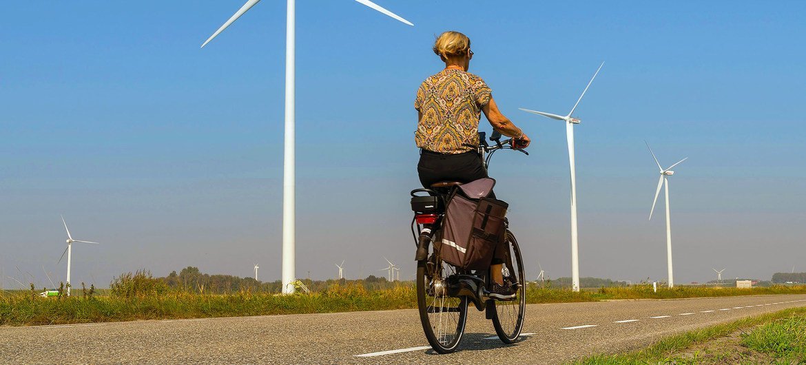 Una mujer pasa en bicicleta junto a unos turbinas eólicas en una carretera rural de Heijningen (Países Bajos).   